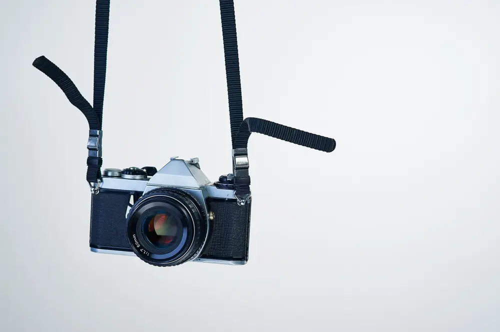 A 35mm film SLR hanging from a neck strap against a white backdrop. Illustration of photography gear minimalism.