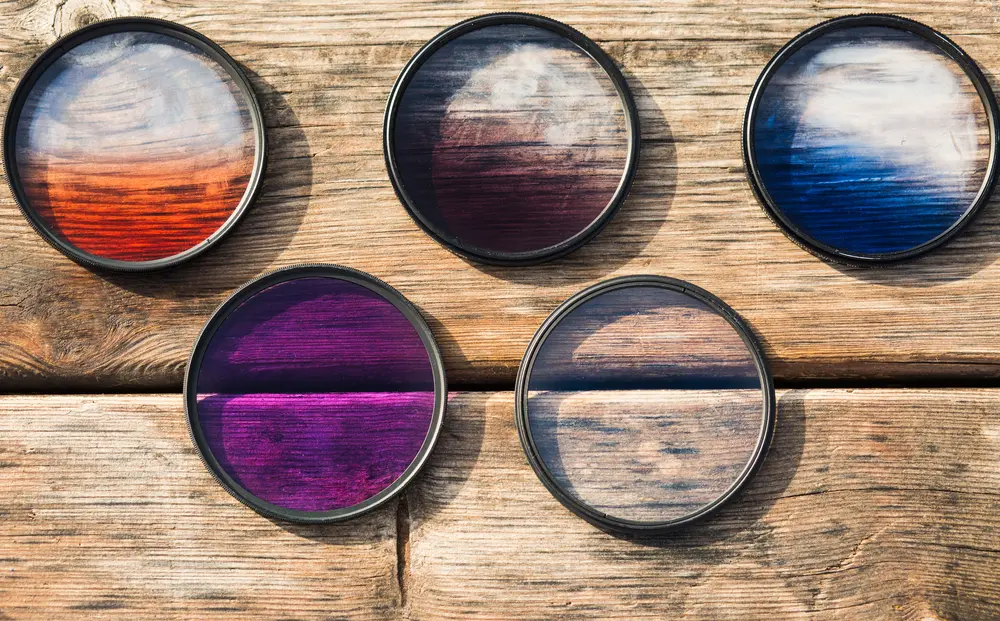 A selection of lens filters for creative use on a wooden table backdrop.