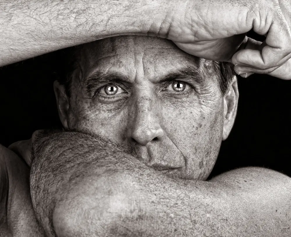Fine art portrait of middle-aged man looking into the camera. Black-and-white exposure, using arms to frame face.