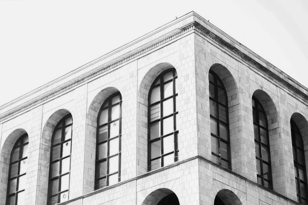 Corner of large building in high-key lighting, rounded tall windows.