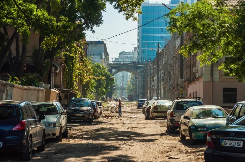 Street photography of empty road, parked cars and lone woman in middleground.