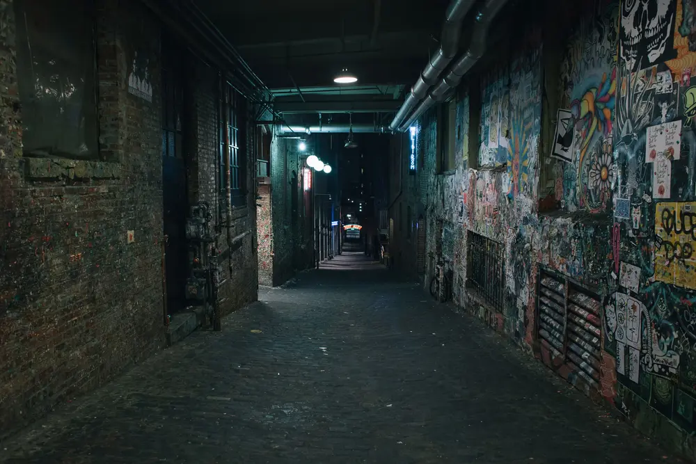 Dark, grafitti-lined alleyway underground. Street photography in color in low light.