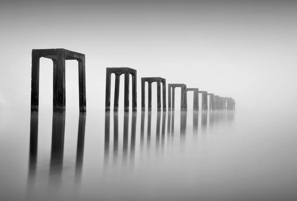 Abstract photography, landscape in black and white. Large structures rising out of water in series, leading lines vanishing into horizon.