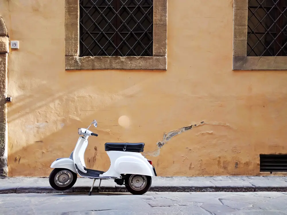 Quiet street scene, Vespa scooter parked next to old-style facade. Empty streets.