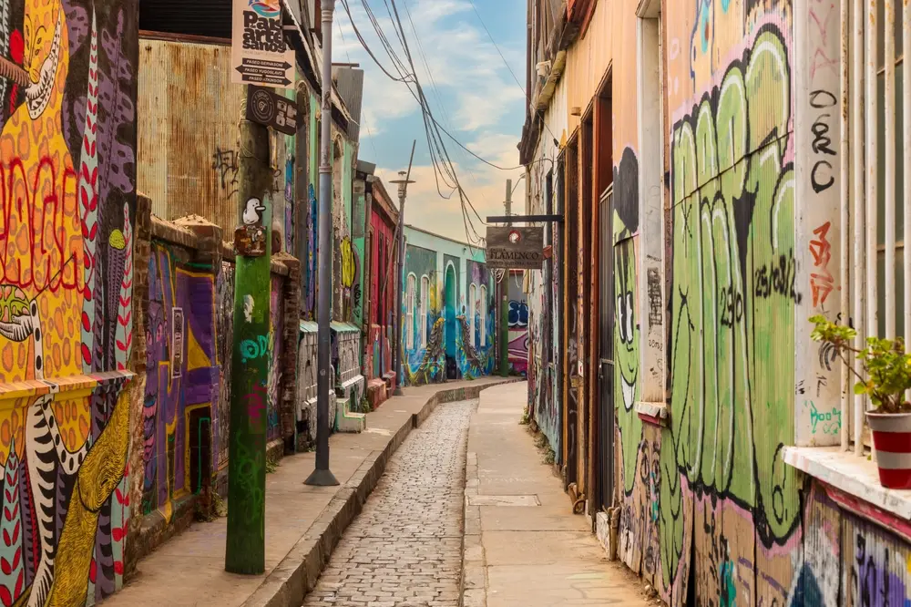View of narrow alleyway in urban environment. Street art lining the facades and lampposts.