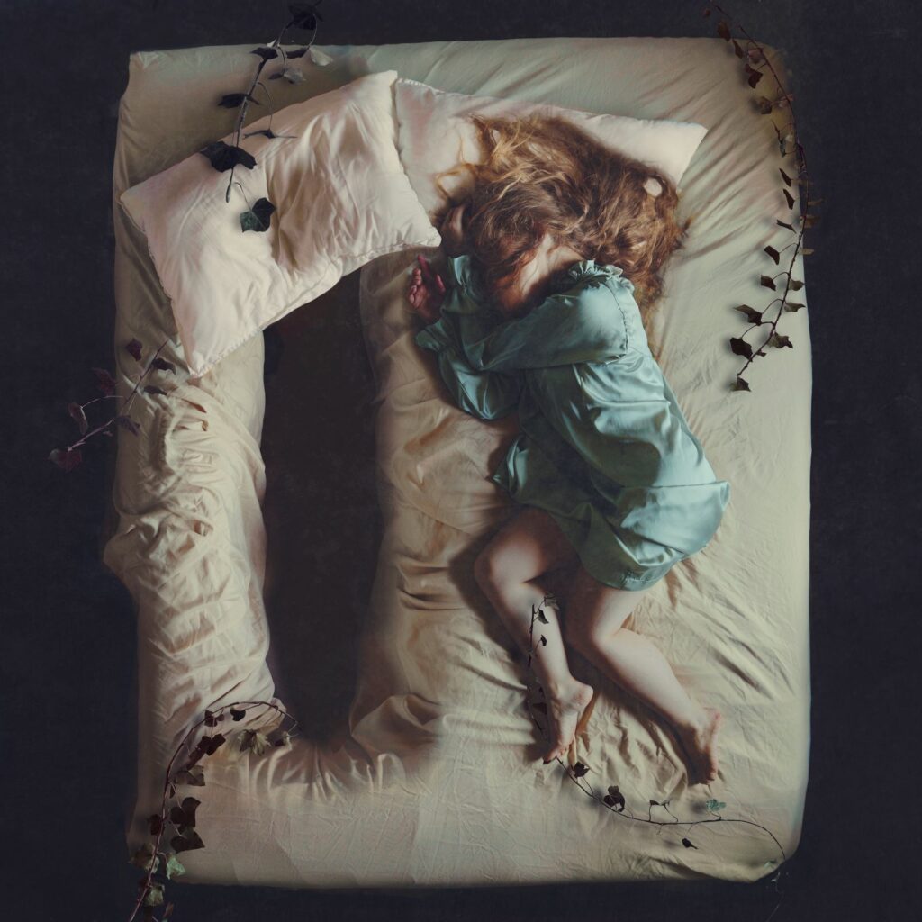 An image of a woman laying in a bed with a giant hole beside her by Brooke Shaden.