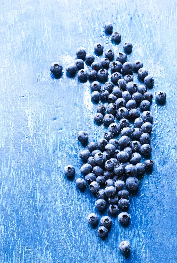 Blueberries scattered across a textured blue surface with strong use of negative space.