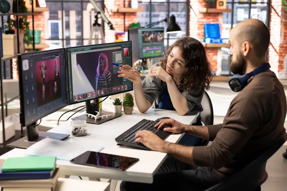 Two individuals working with a photo editor software on a desktop computer. Photography and post-processing concept.