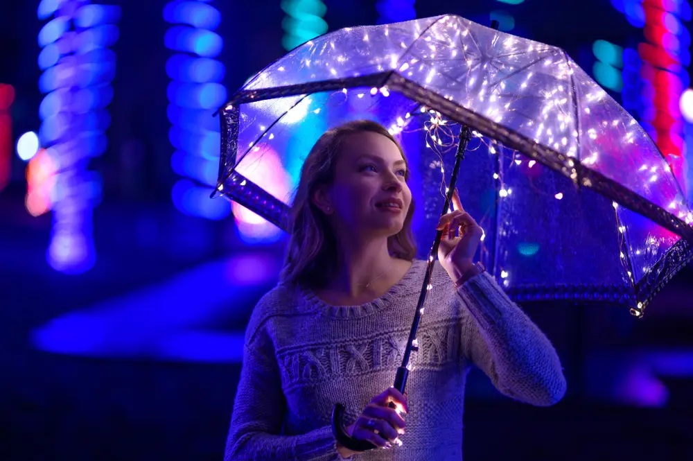 Low-light portrait photography in color. Woman holding umbrella standing in front of city lights at night.