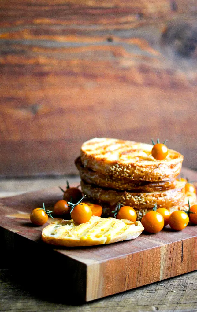 Stacked slices of grilled bread topped with golden cherry tomatoes on a wooden cutting board.