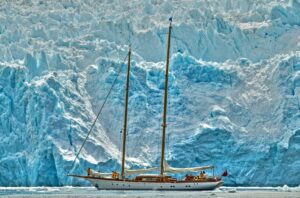 A photo of a sailboat in front of an iceberg.