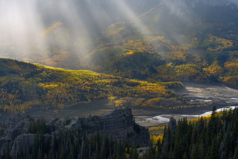 A landscape photography drone image of sun rays lighting up an mountainous region.