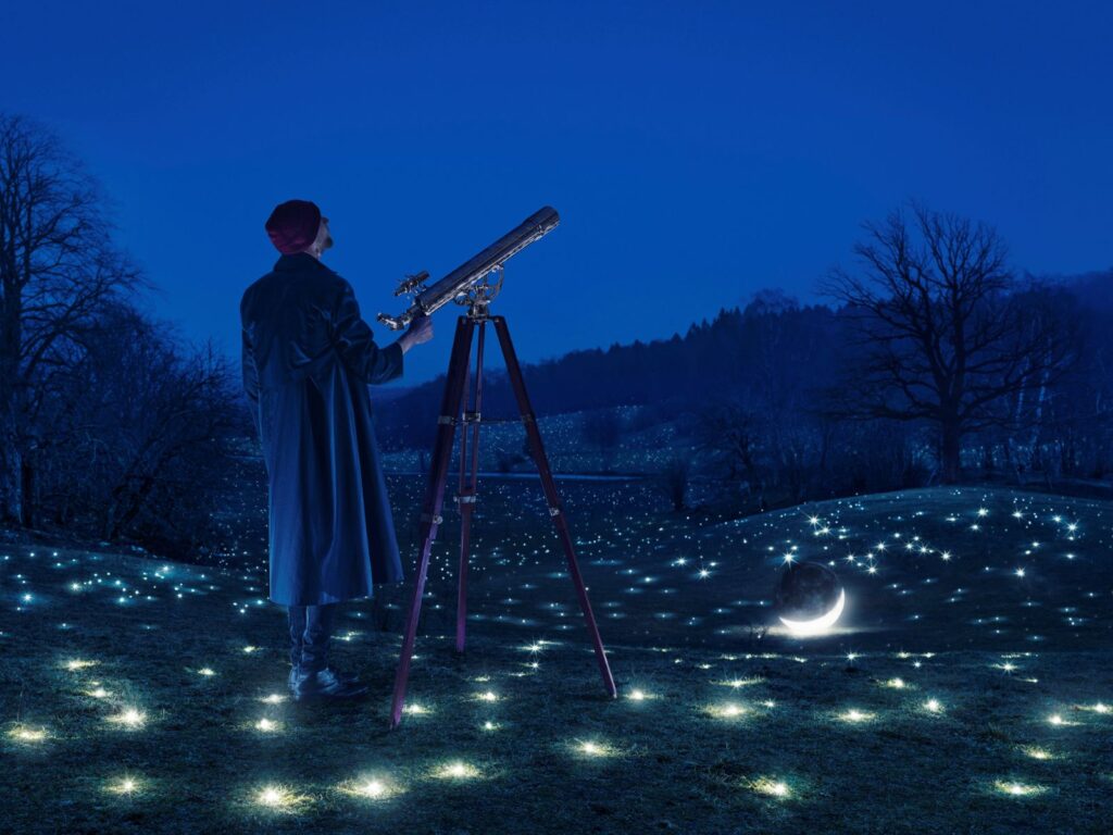 A surreal image of someone aiming a telescope at the sky while the stars and moon are on the ground at his feet by Erik Johansson.