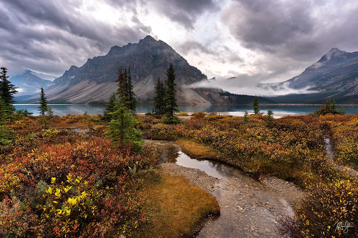 Moody autumn scene at Bow Lake with misty mountains and still water in Banff National Park.
