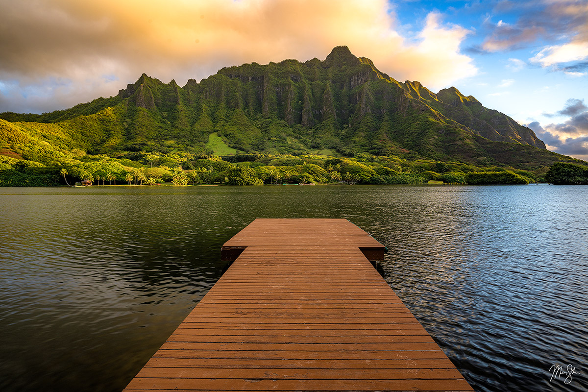 Wooden pier leading toward the lush Koʻolau mountains under soft sunset light on Oahu.