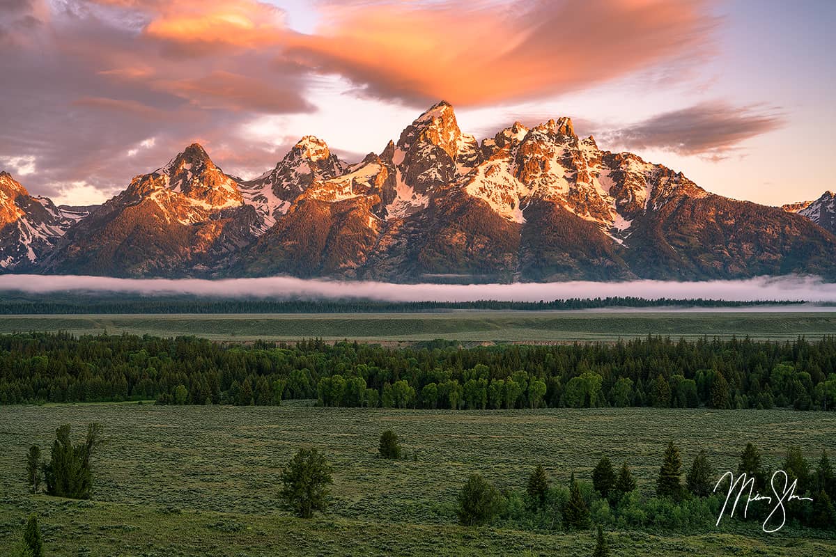 Sunrise glow on the Teton Range above forests and open meadows in Wyoming.