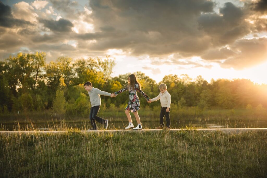 An image of a family holding hands as they walk along a path during golden hour, photographed by Kristeen Waddell.