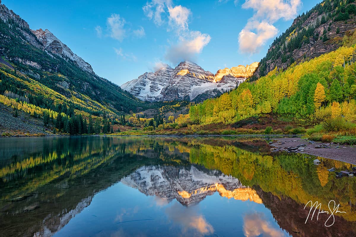 Calm lake reflecting the Maroon Bells and colorful autumn slopes in Colorado.