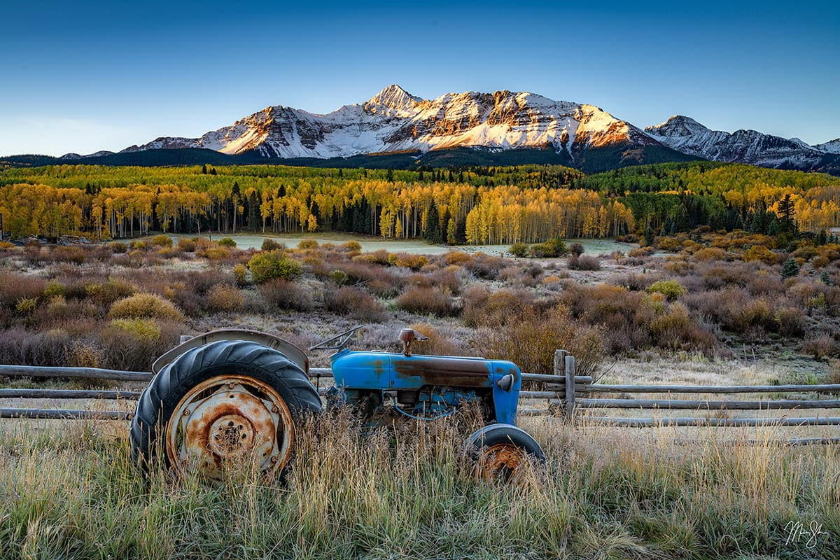 Rusty blue tractor in a fall meadow with Mount Wilson lit by sunrise in the background.