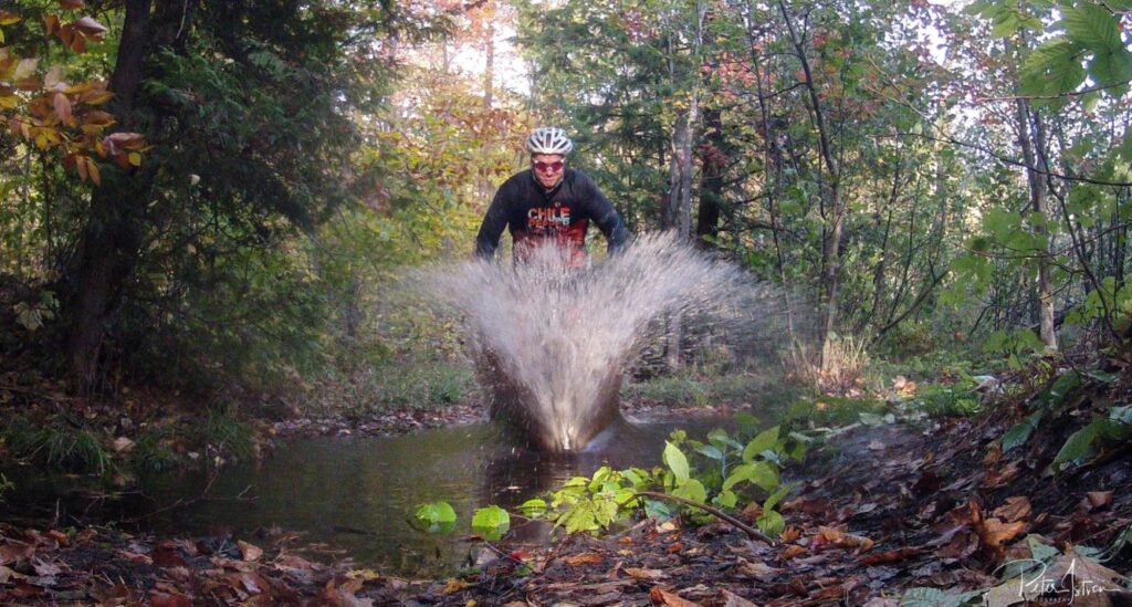 An image of Peter riding through a deep puddle in a forest on his bike.