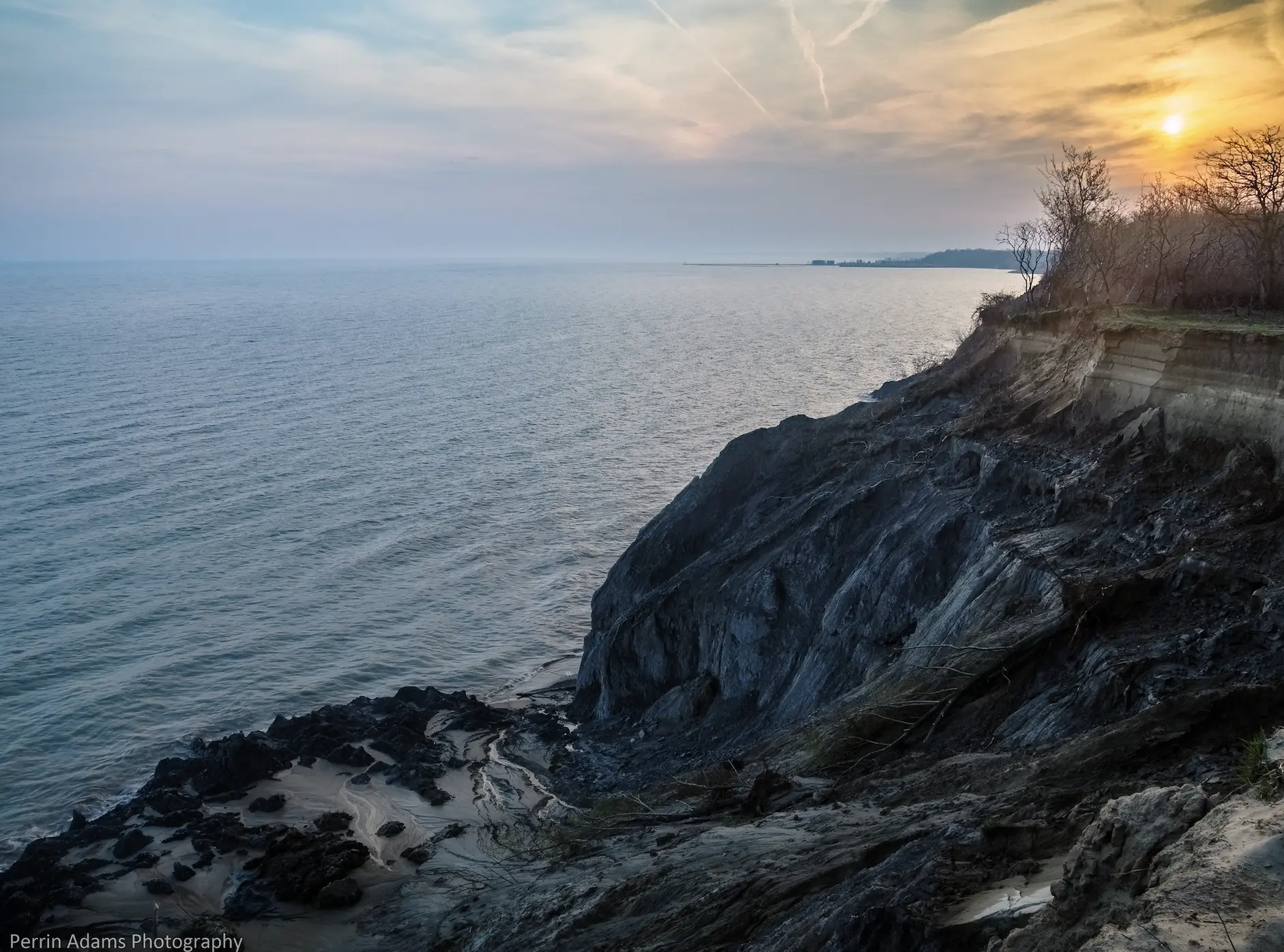 Rocky shoreline sweeping diagonally toward the horizon at sunset, creating a strong leading line that guides the viewer’s eye into the image.