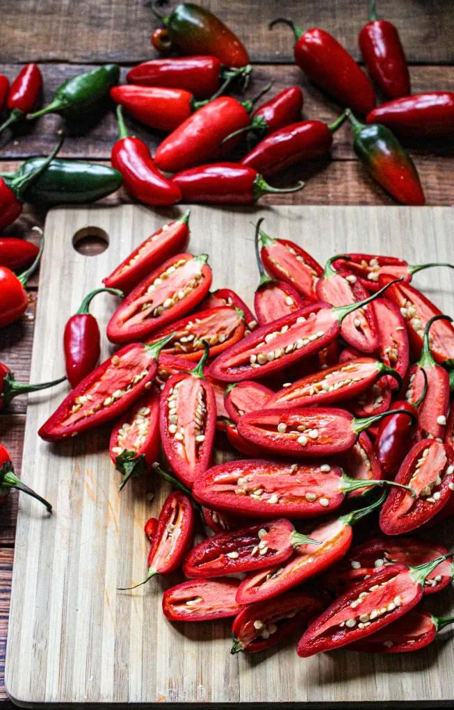 Overhead view of fresh jalapeños, whole and sliced, arranged on a cutting board for a food photography setup.