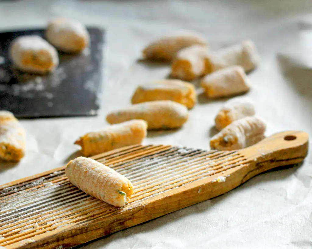 Homemade gnocchi pieces dusted with flour on a wooden gnocchi board, showing a work-in-progress food preparation scene.