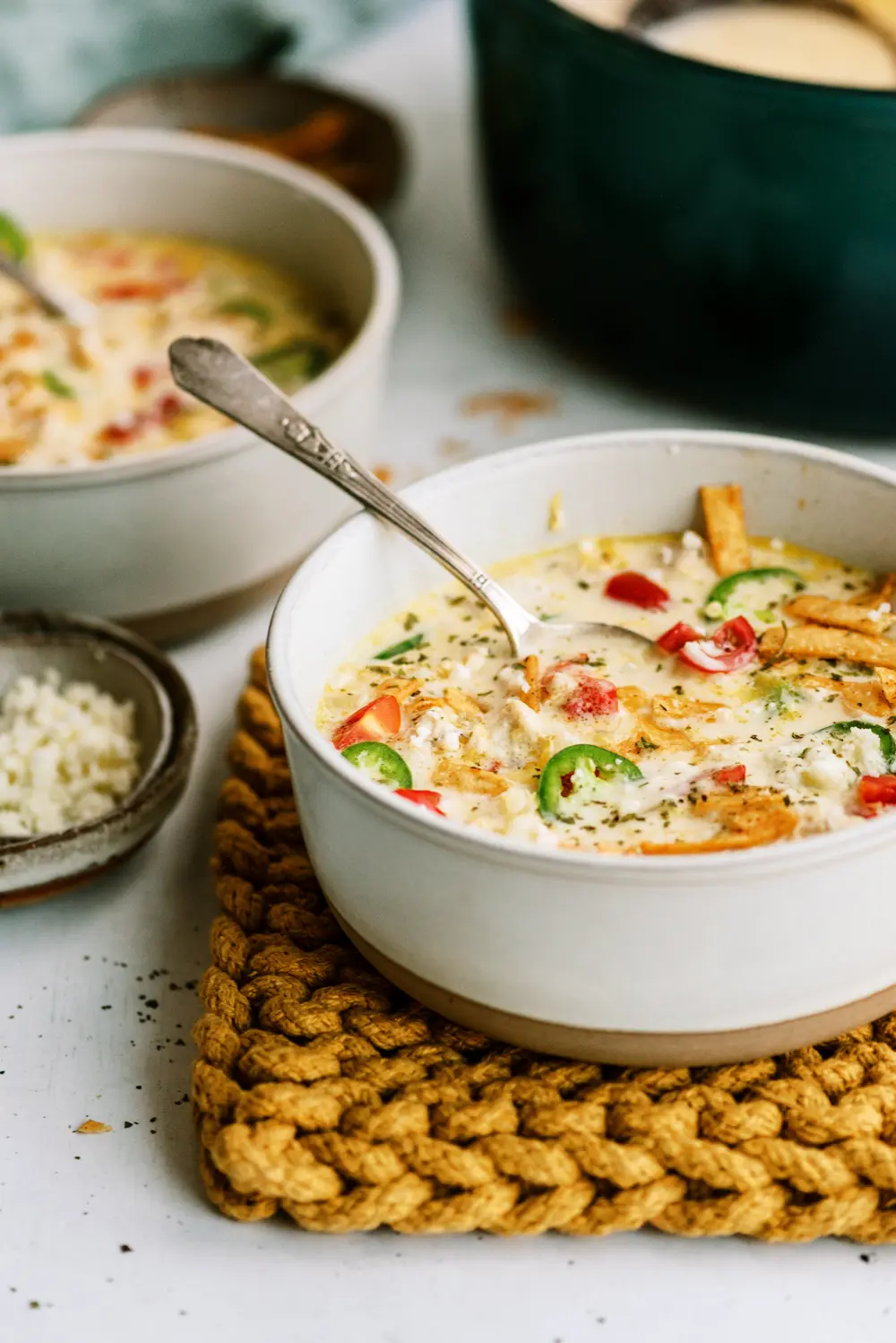 Chicken tortilla soup styled with a spoon, secondary bowls, and background elements to demonstrate layering and depth.