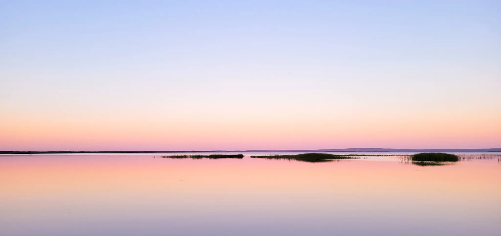 Pastel sunset over the calm waters of Lake Superior with small islands surrounded by wide negative space.