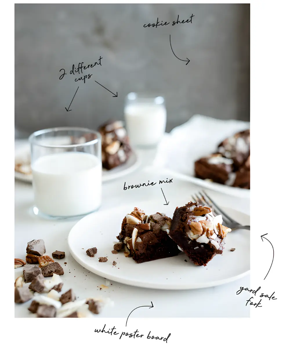 Food photography practice scene showing brownies on a white plate styled with mismatched cups, crumbs, a fork, and a cookie sheet using natural light.