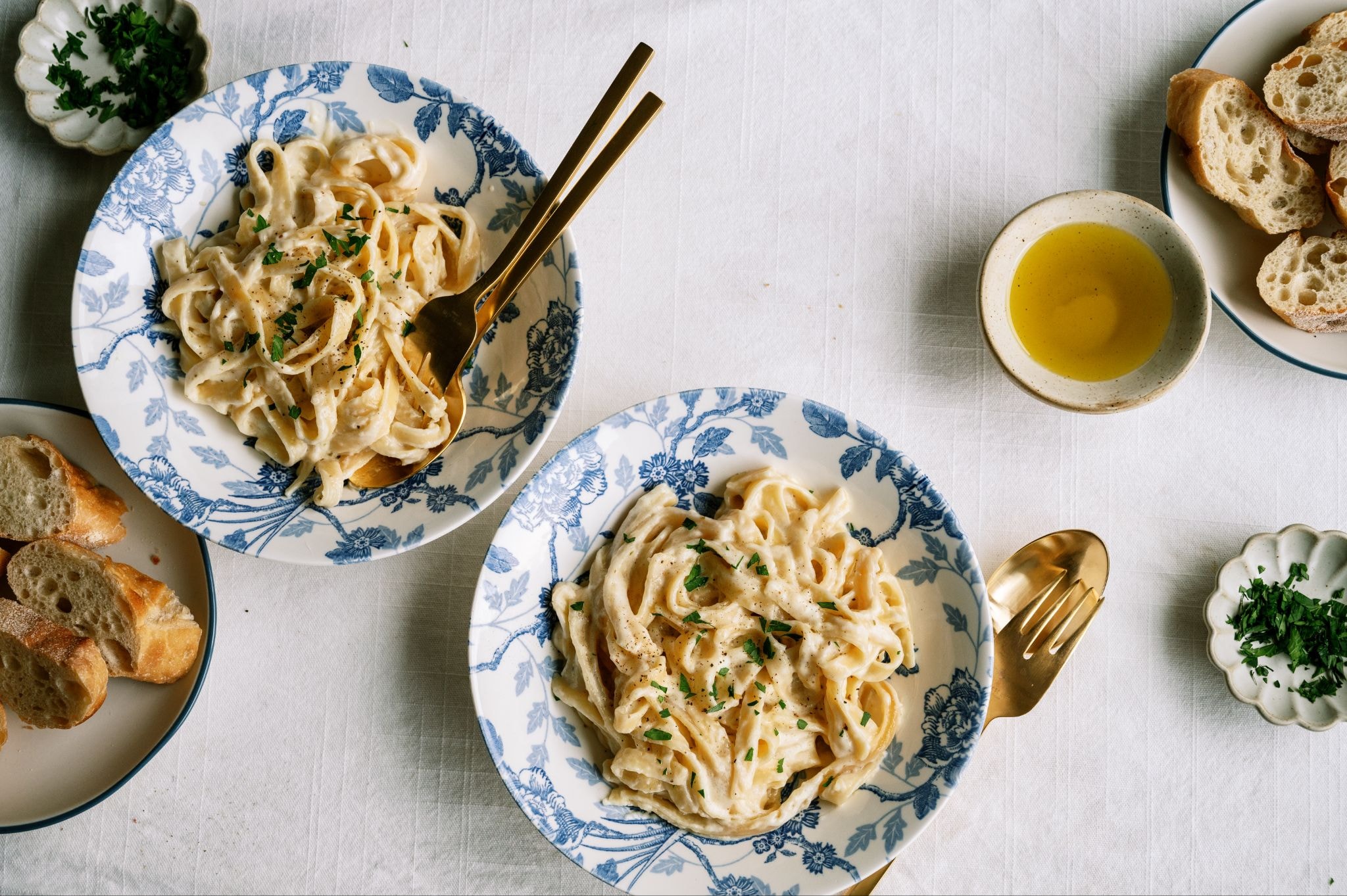 Overhead food photograph of pasta plates lit from the side by natural window light, creating soft shadows and visible texture.