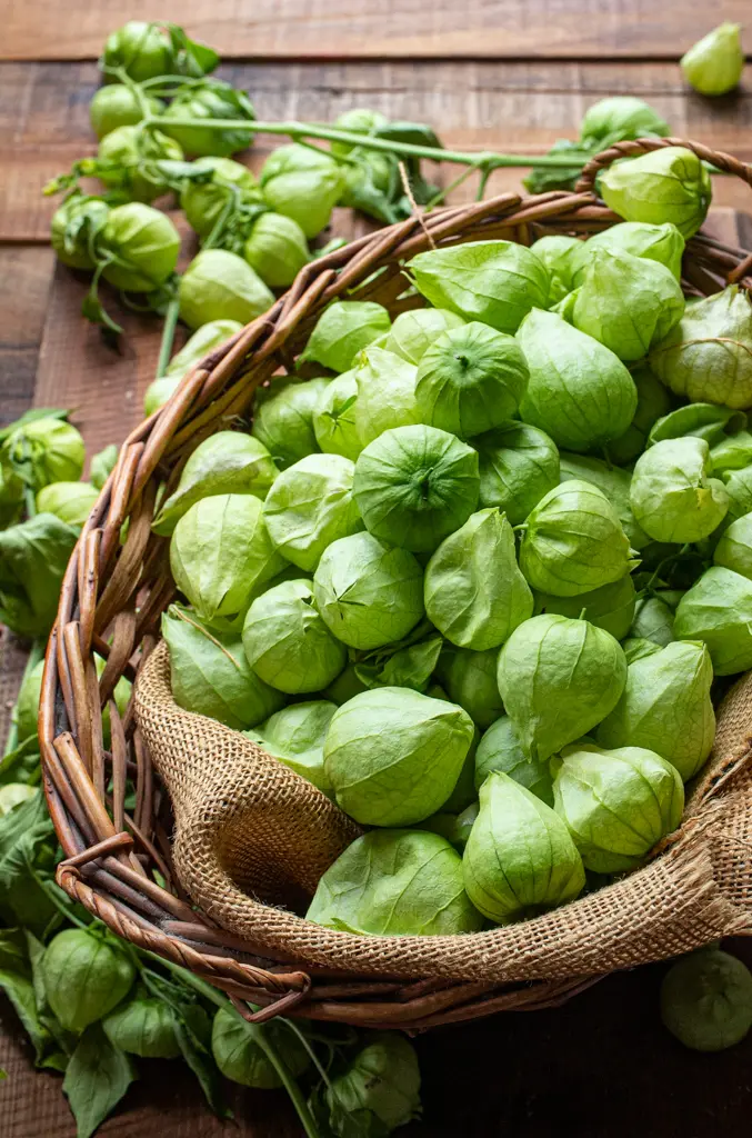 Fresh green tomatillos piled in a woven basket on a rustic wooden table.