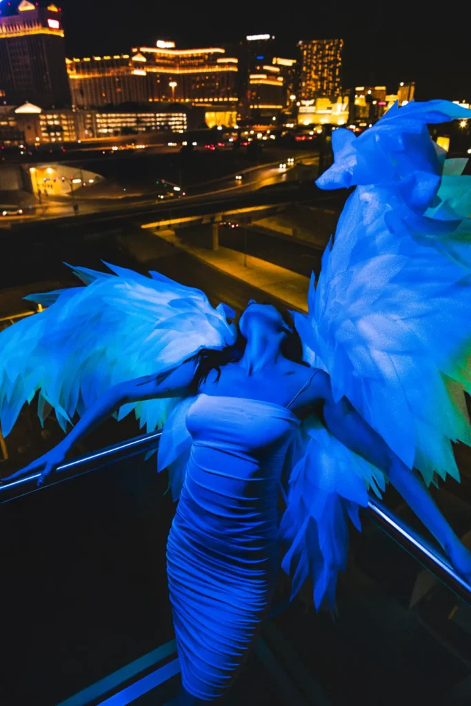 An image of a woman with angel wings leaning against a balcony at night by Sin City Creative.