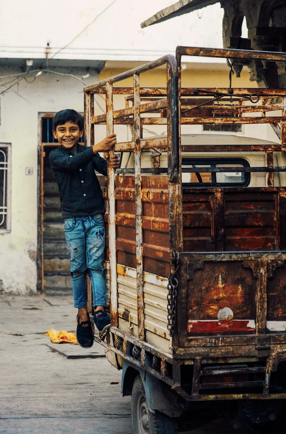 Young boy smiling while climbing onto the back of a small truck in India.