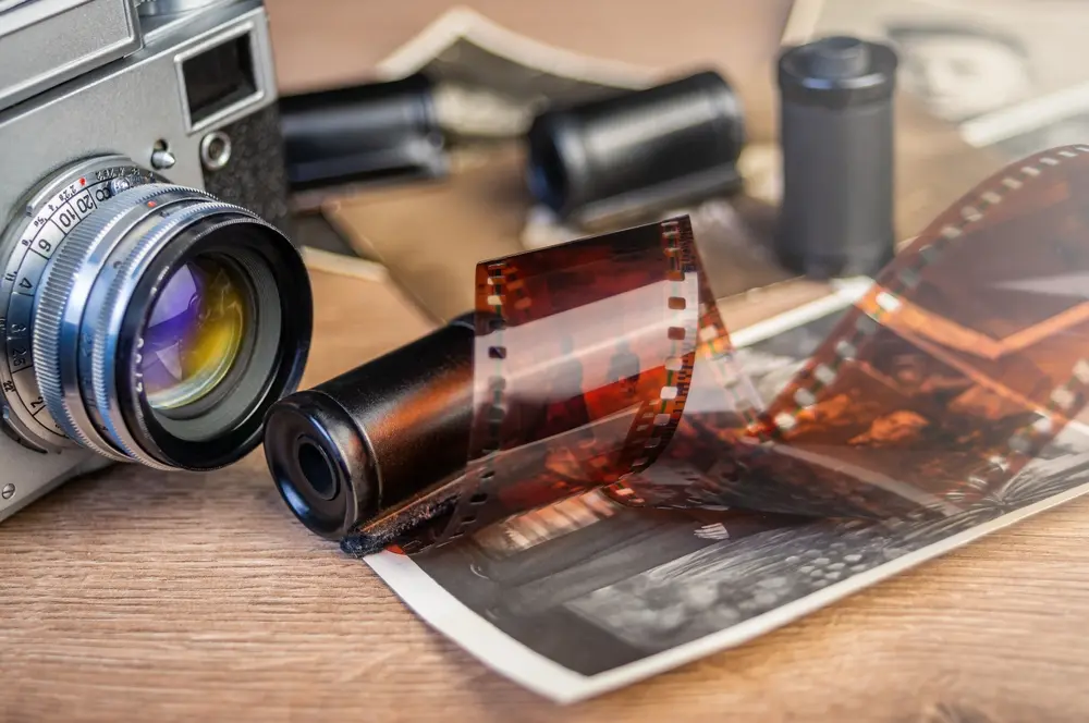 Vintage film camera with 35mm film roll and developed photo on a wooden table.