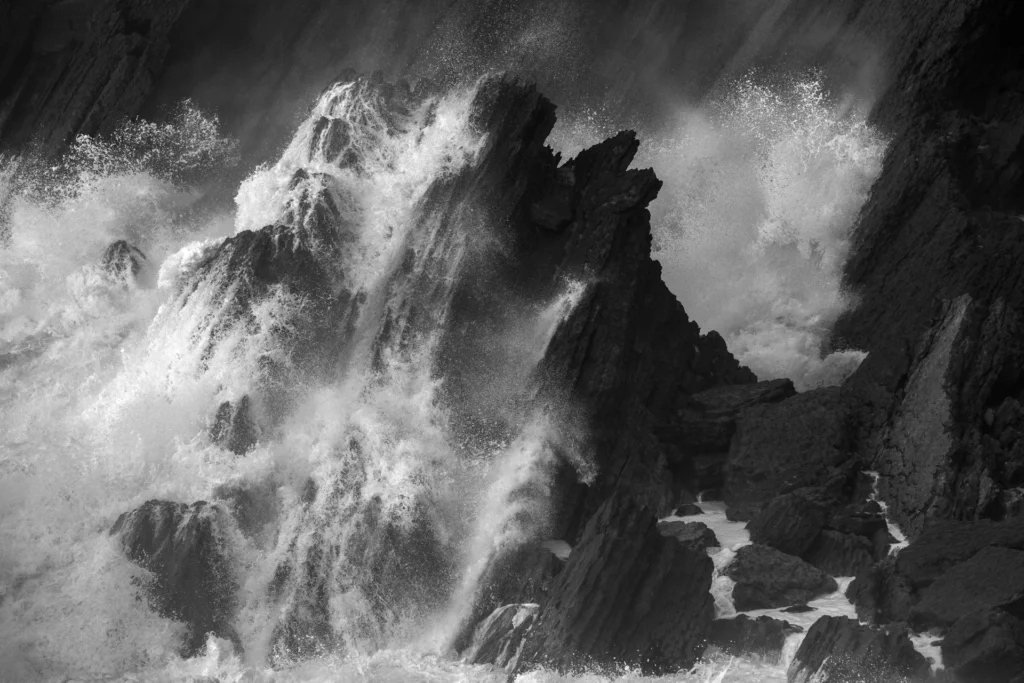 An image of waves crashing into a dark rock wall by Rachael Talibart