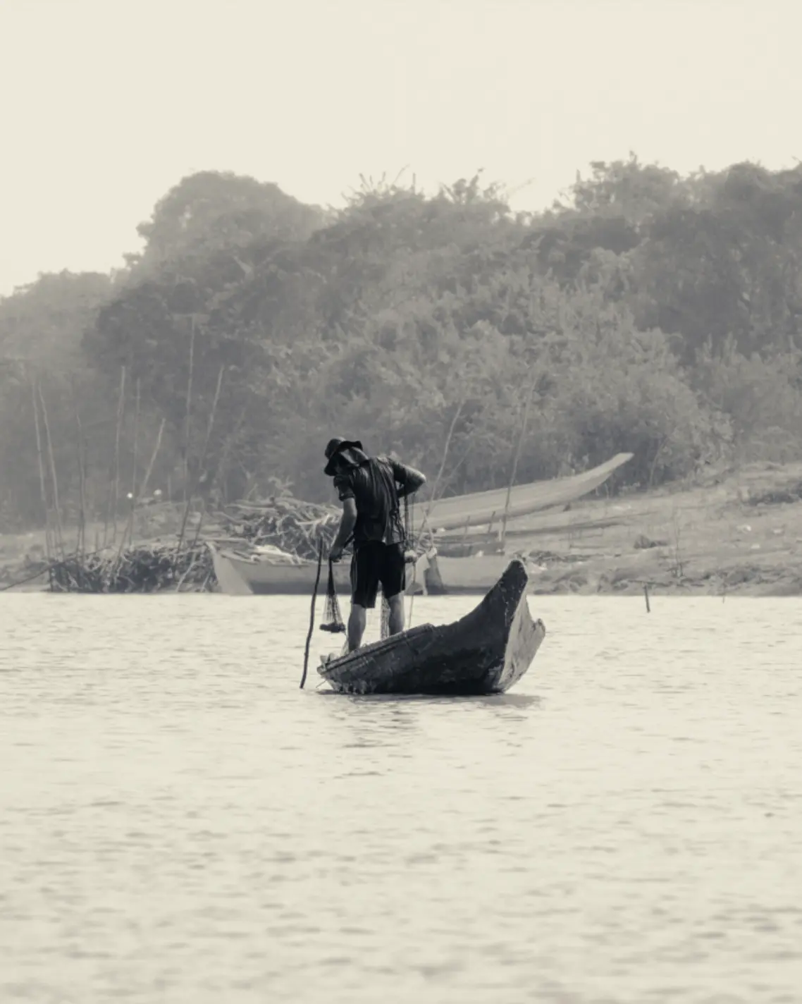 Fisherman standing on a narrow wooden boat on Tonle Sap Lake in Cambodia.