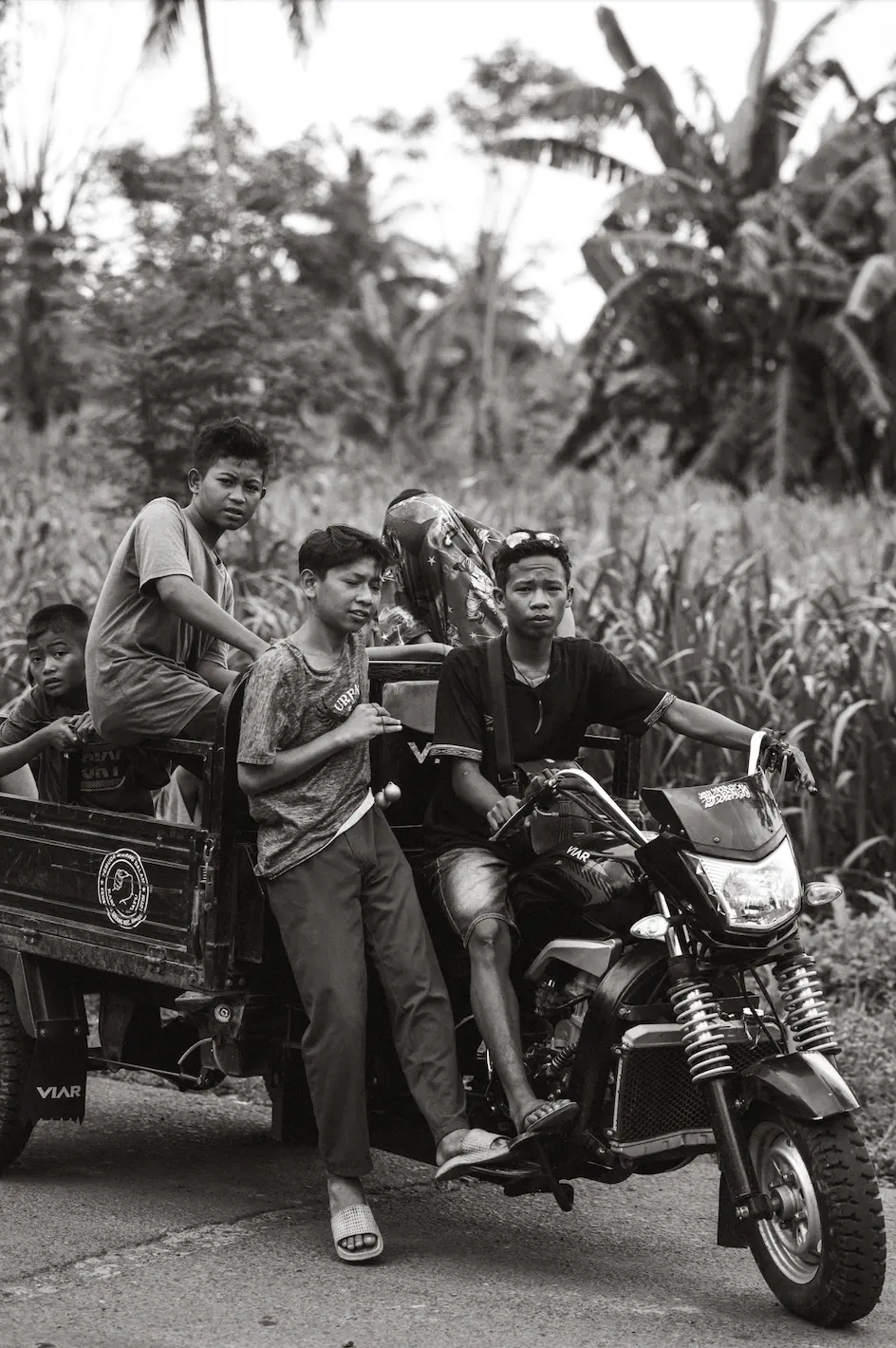 Group of young men riding a motorbike pulling a small cart on a rural road in Indonesia.