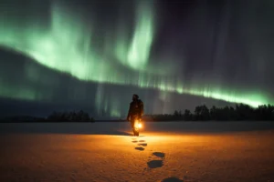 An image of a person standing under some northern lights in a snowy field holding a lantern by Matti Seppänen