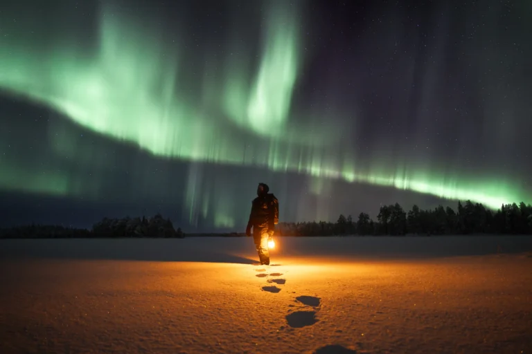 An image of a person standing under some northern lights in a snowy field holding a lantern by Matti Seppänen
