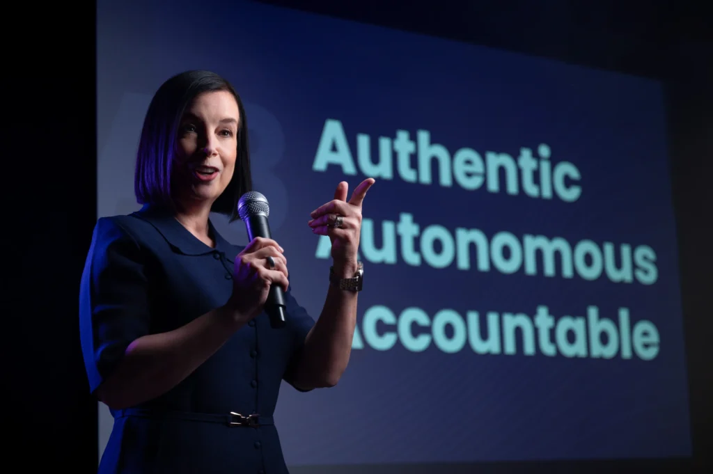 A corporate portrait of a woman talking on stage by Daniel Wakefield.