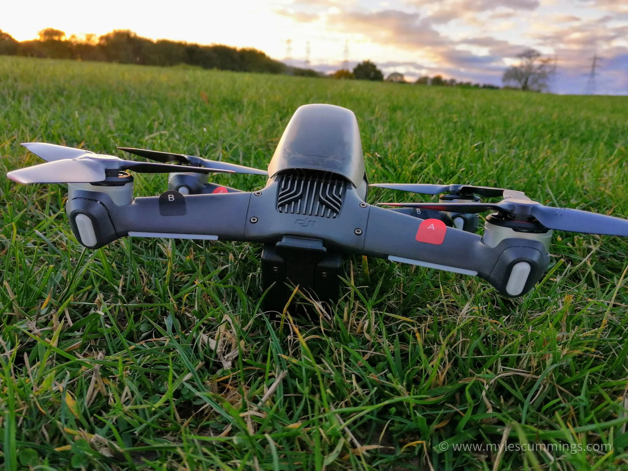 A grey DJI-style camera drone on grass in warm early-morning light