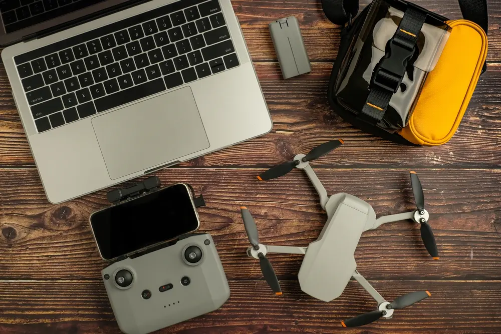 A laptop, drone controller, and folded drone on a wooden editing desk