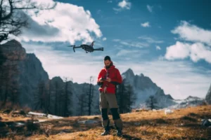 A photographer in a red jacket standing on a clifftop overlooking a dramatic mountain landscape