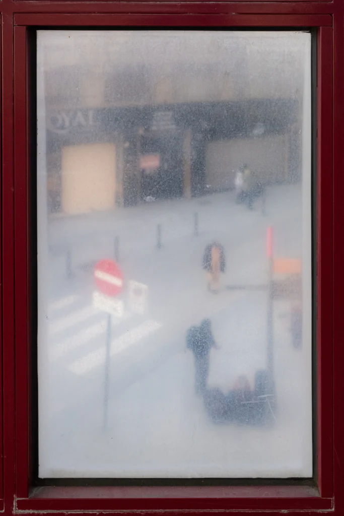 A street photography image through a dusty old window by Frederic Paulussen.