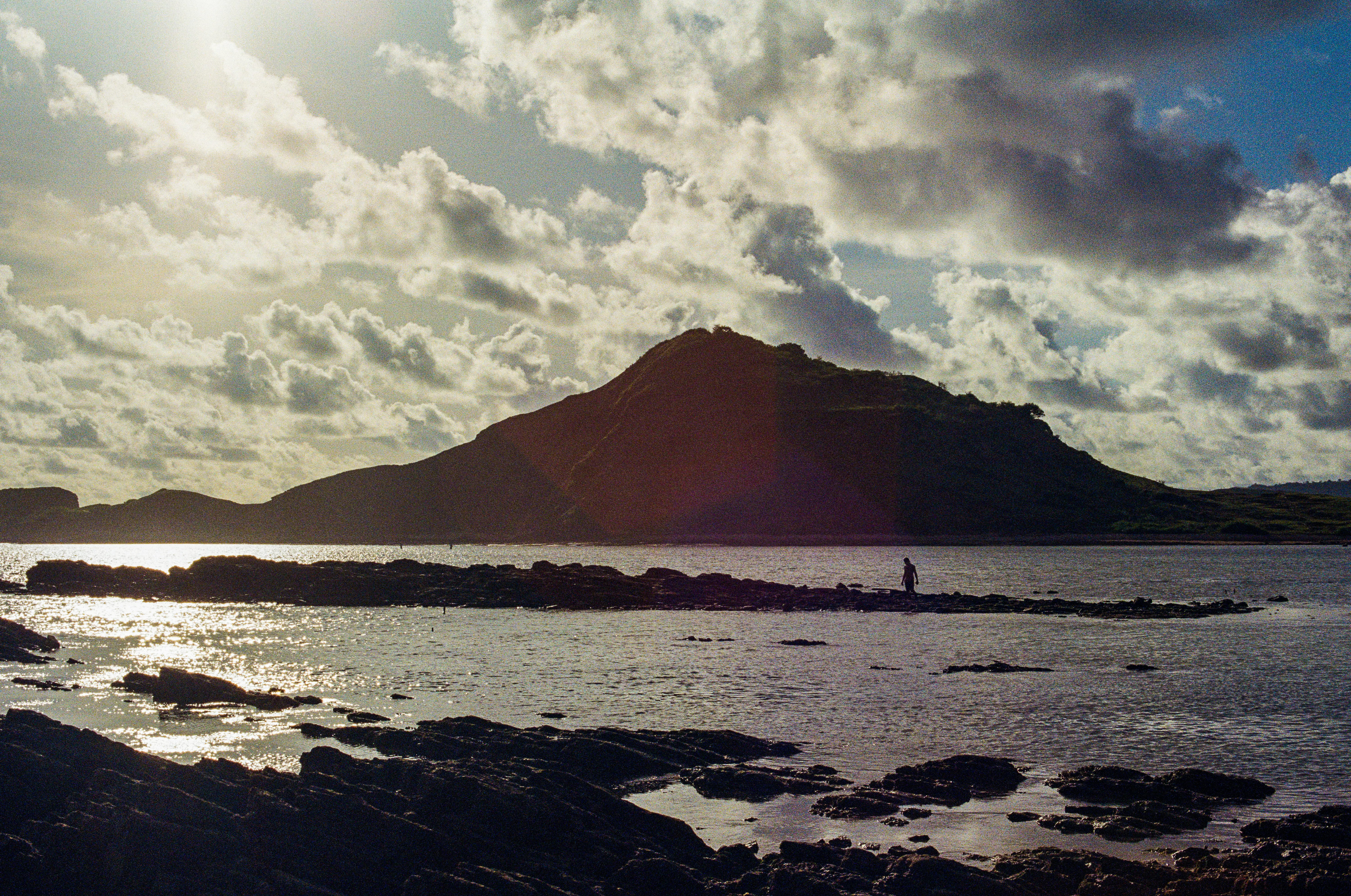 Lone figure walking across rocks at dusk below a silhouetted headland on the coast of Lombok, Indonesia