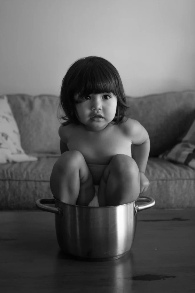 A photo of a small child sitting in a cooking pot by Antoine Didienne.